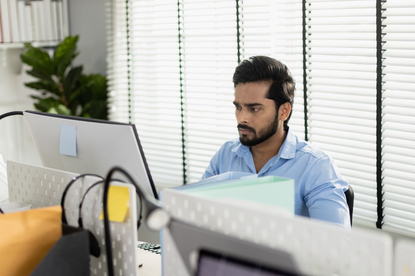 A man at an office desk looking at his monitor, a headset hanging on the stand in front of him