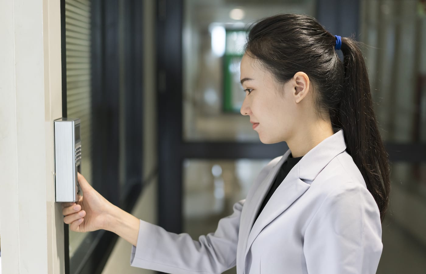 A woman pressing her finger to a wall-mounted fingerprint reader beside a glass door