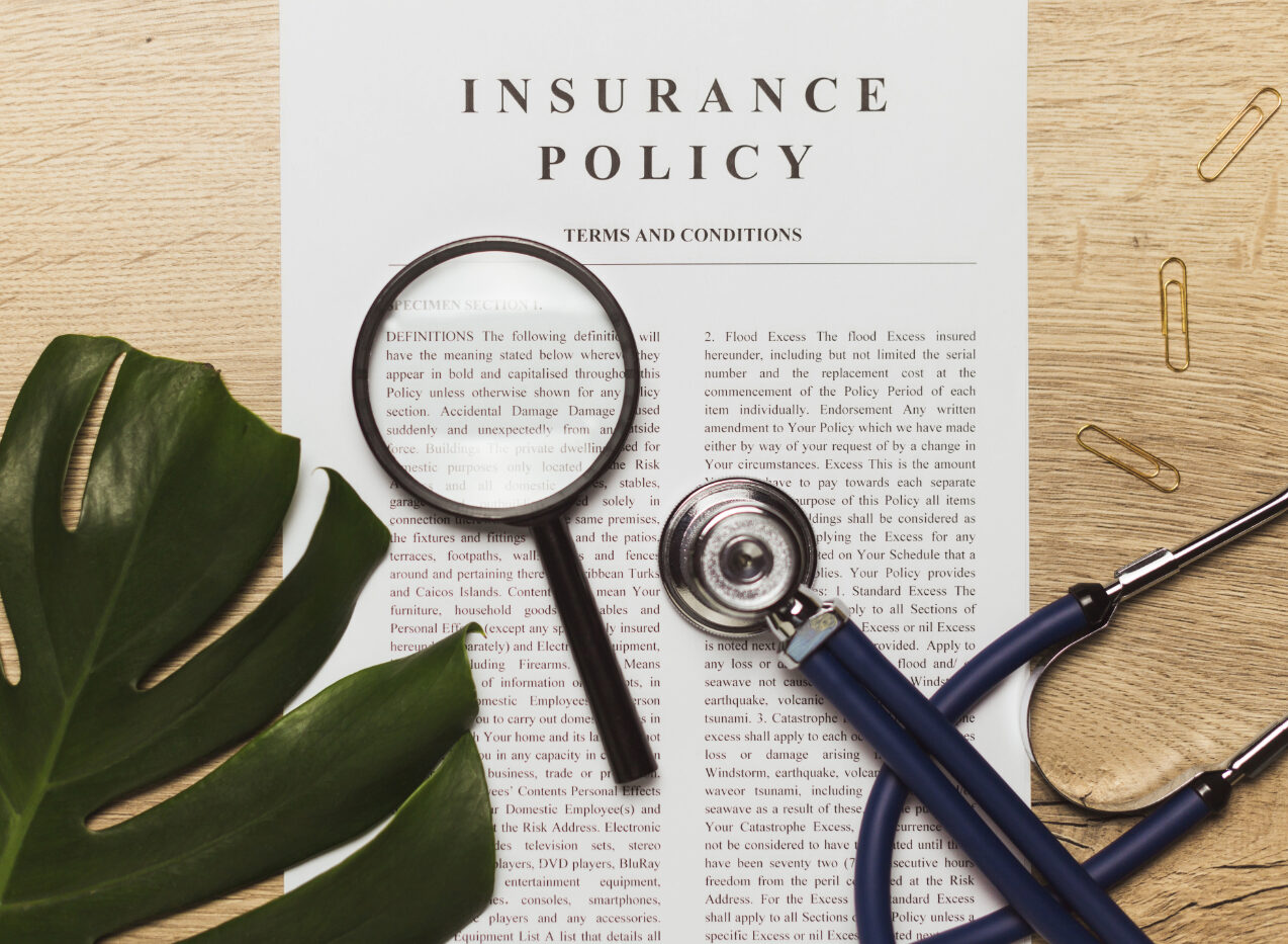 A printed insurance policy under a magnifying glass beside a stethoscope