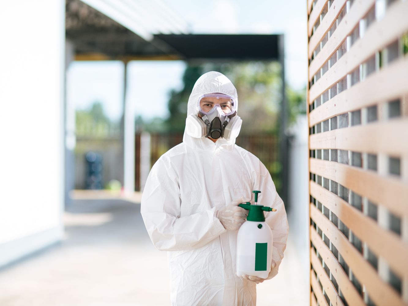 A pest-control technician in a protective suit and respirator holding a hand sprayer