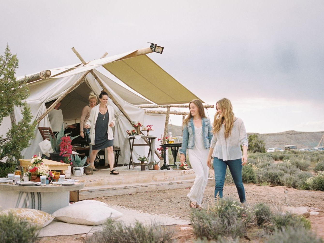 Guests walking past large canvas tents with outdoor seating at a camp in open countryside