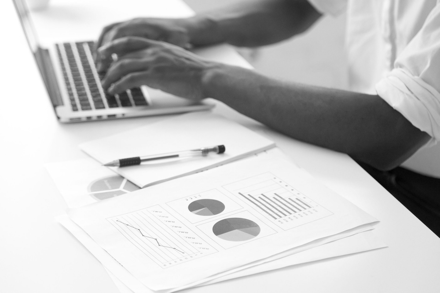 Hands typing on a laptop beside printed charts