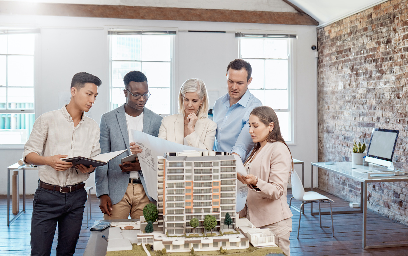 Five colleagues gathered around an architectural model of an apartment block, studying plans and notes