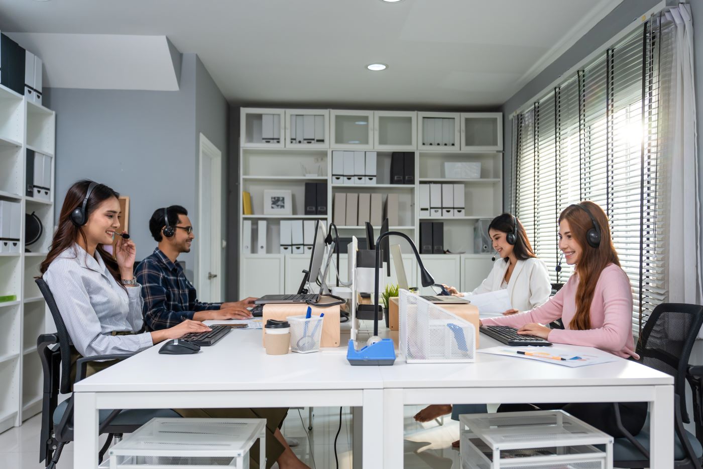 Colleagues in headsets working at computers around a shared desk in a bright office