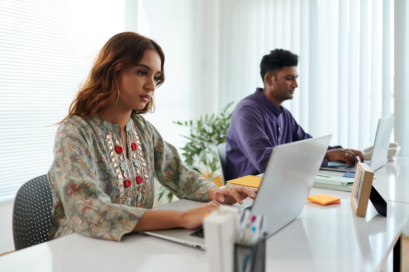 Two colleagues working on laptops at a shared office desk