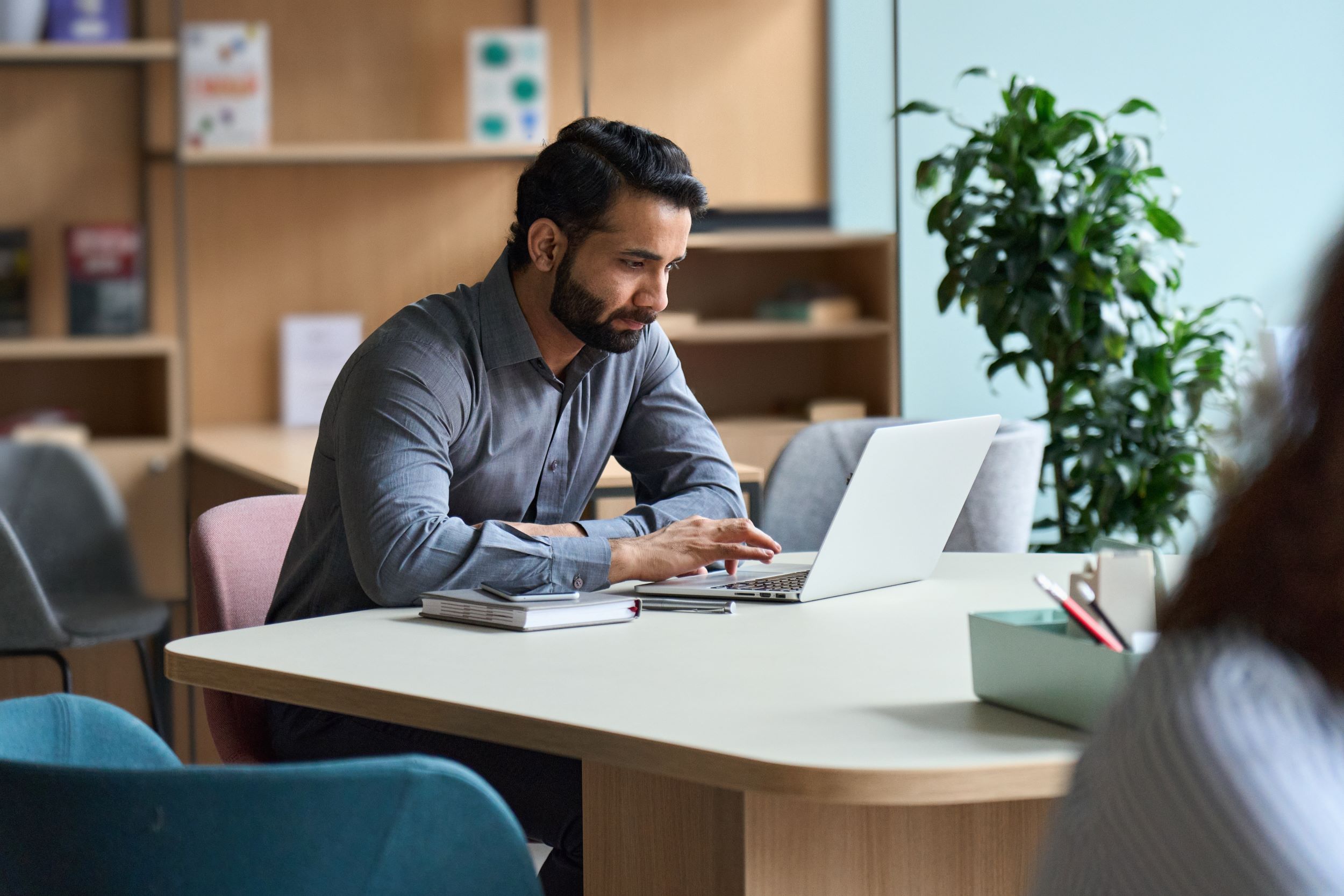 A man working on a laptop at a shared table in a bright office