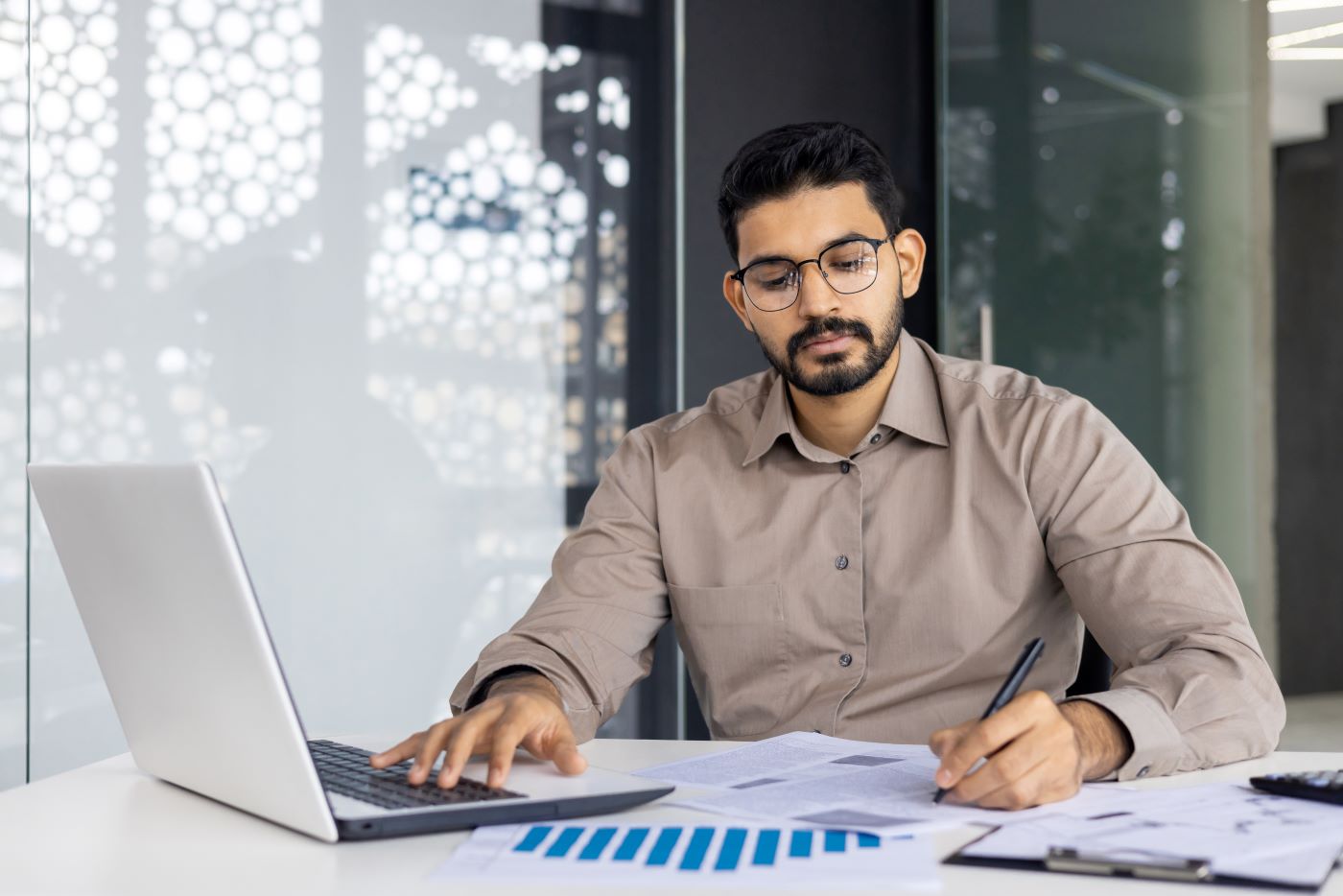 A man working at a laptop beside printed charts