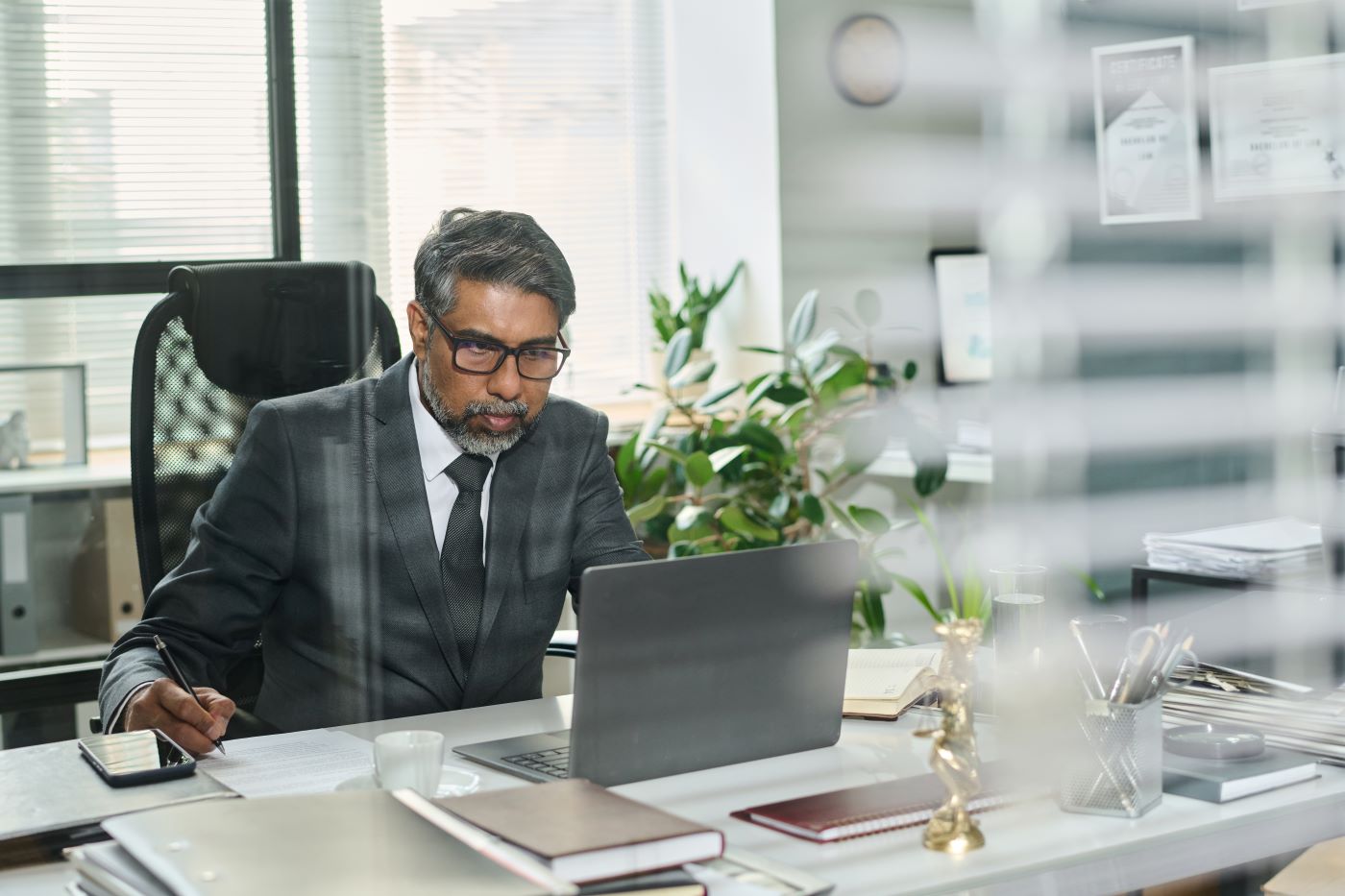 A senior executive in a suit working at a laptop in a private office