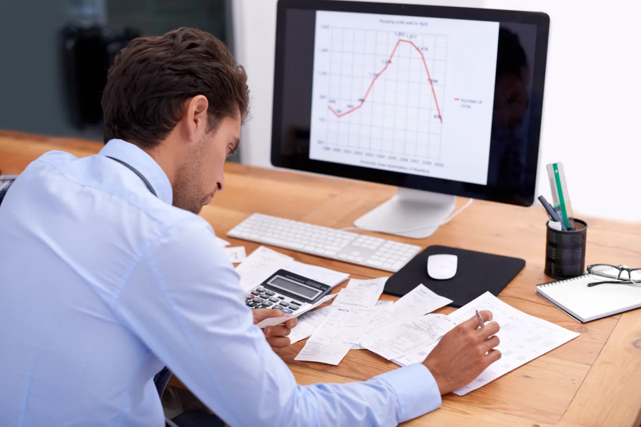 An accountant reviewing figures on screen with a calculator and paperwork