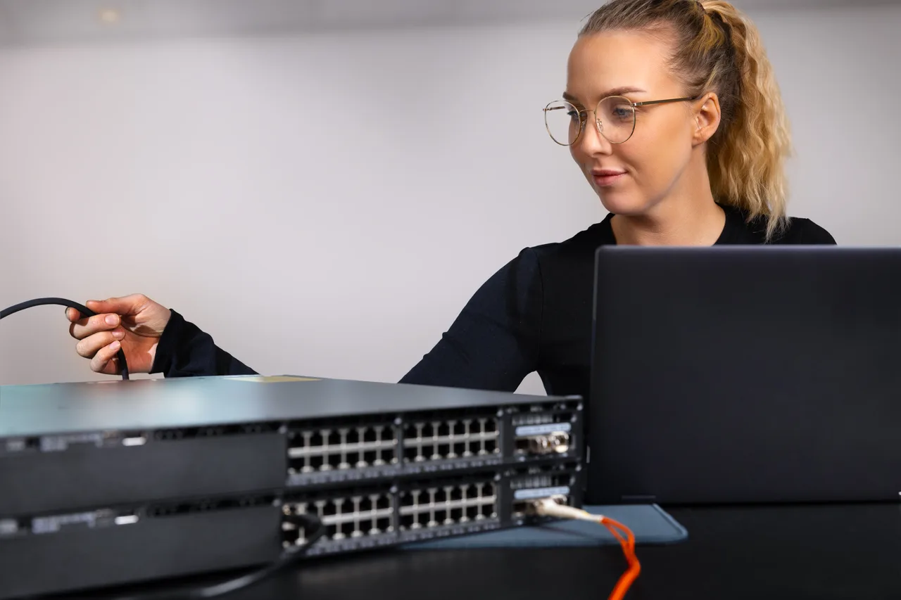 A technician connecting office network equipment beside a laptop