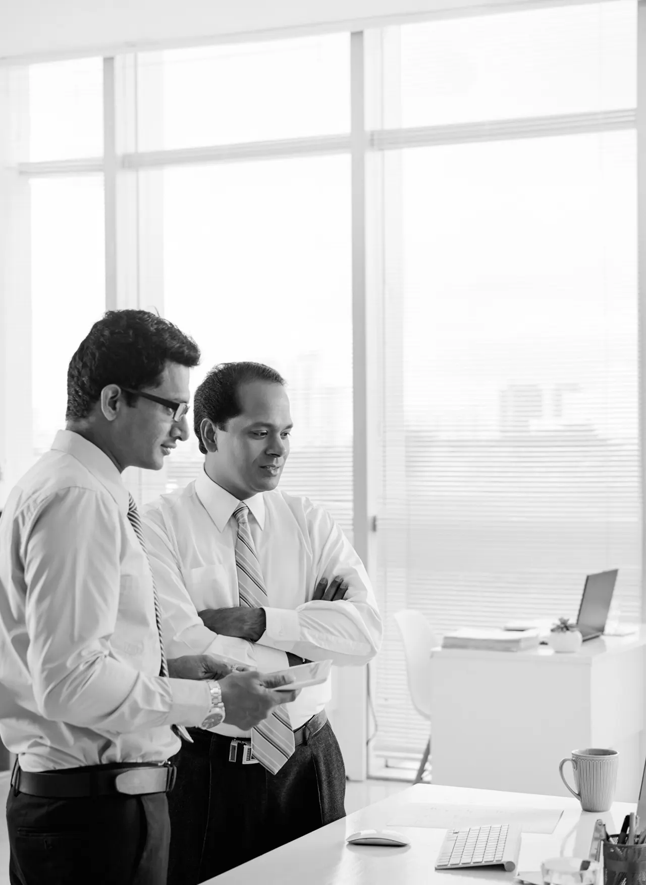 Two colleagues in shirts and ties reviewing a document in a bright office