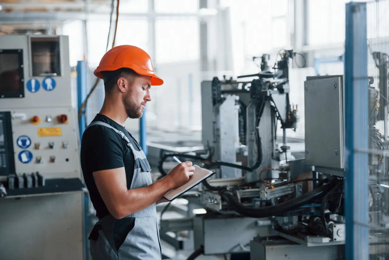 An engineer in a hard hat taking notes beside automated production equipment