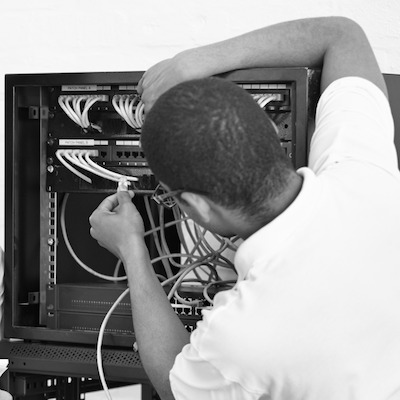 A technician reaching into a network rack to connect patch cables, in black and white