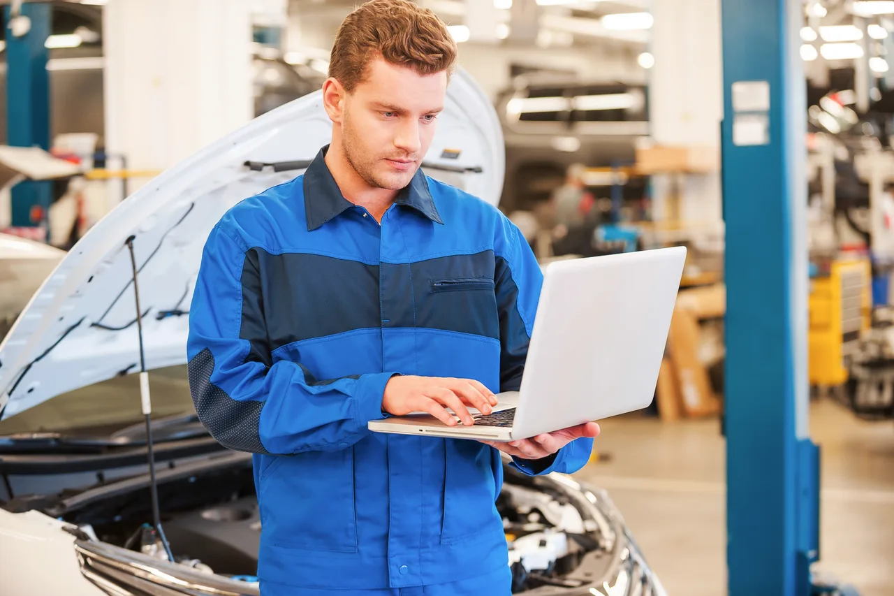 A technician running vehicle diagnostics on a laptop in a workshop