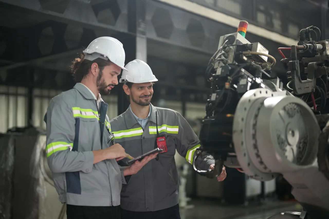 Two engineers in hard hats checking production equipment on a tablet