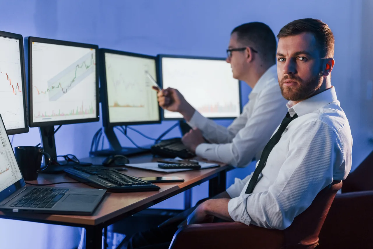 Two analysts monitoring financial data across several screens