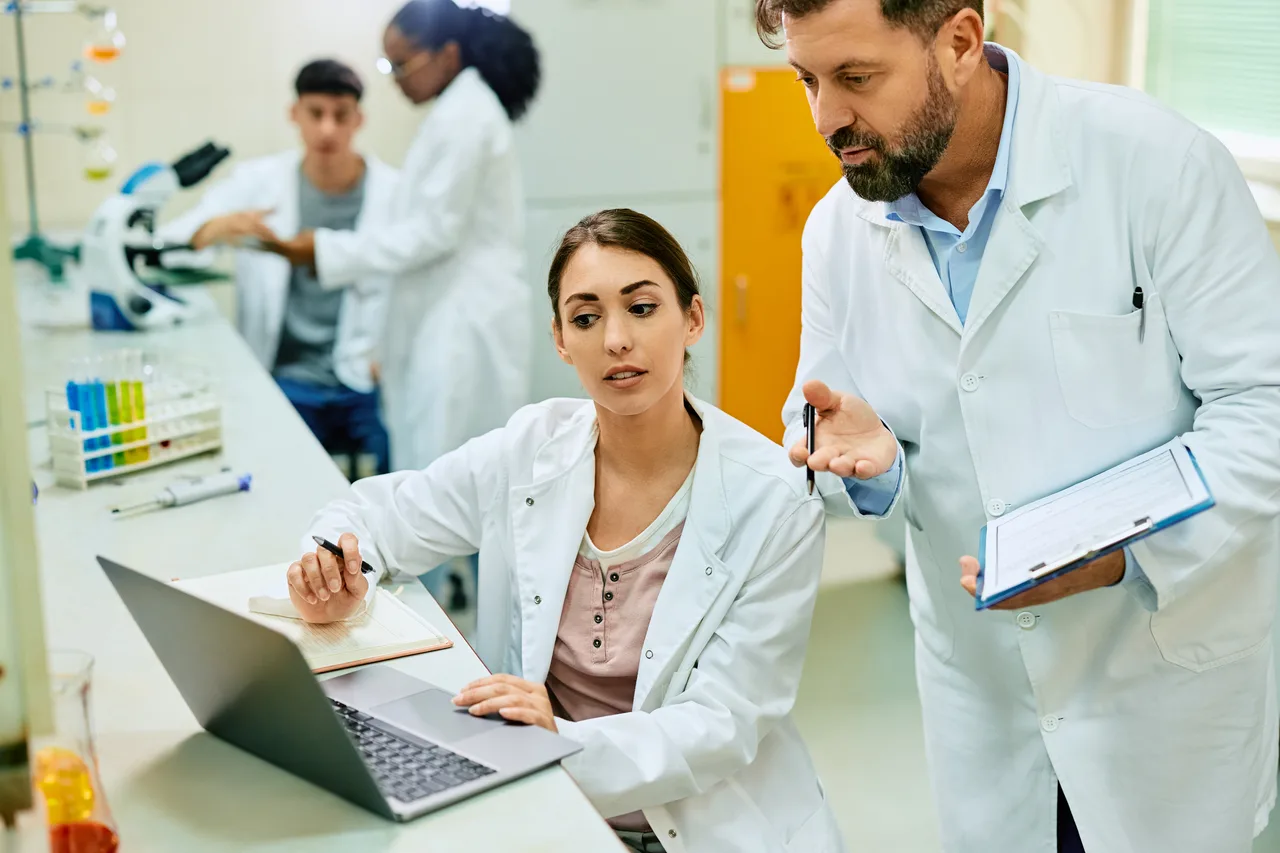 Laboratory scientists reviewing a research project with a clipboard and laptop