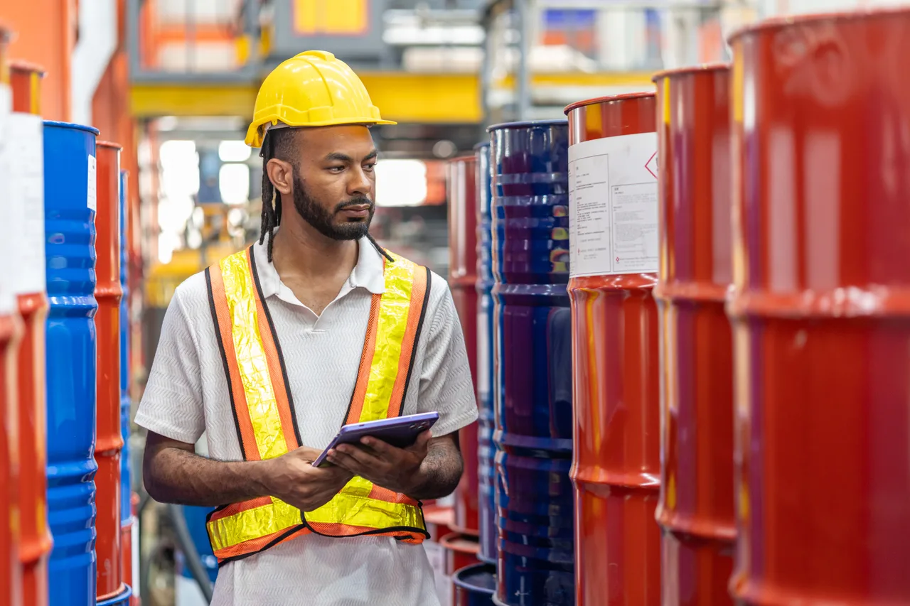 A warehouse worker checking chemical drums against a tablet