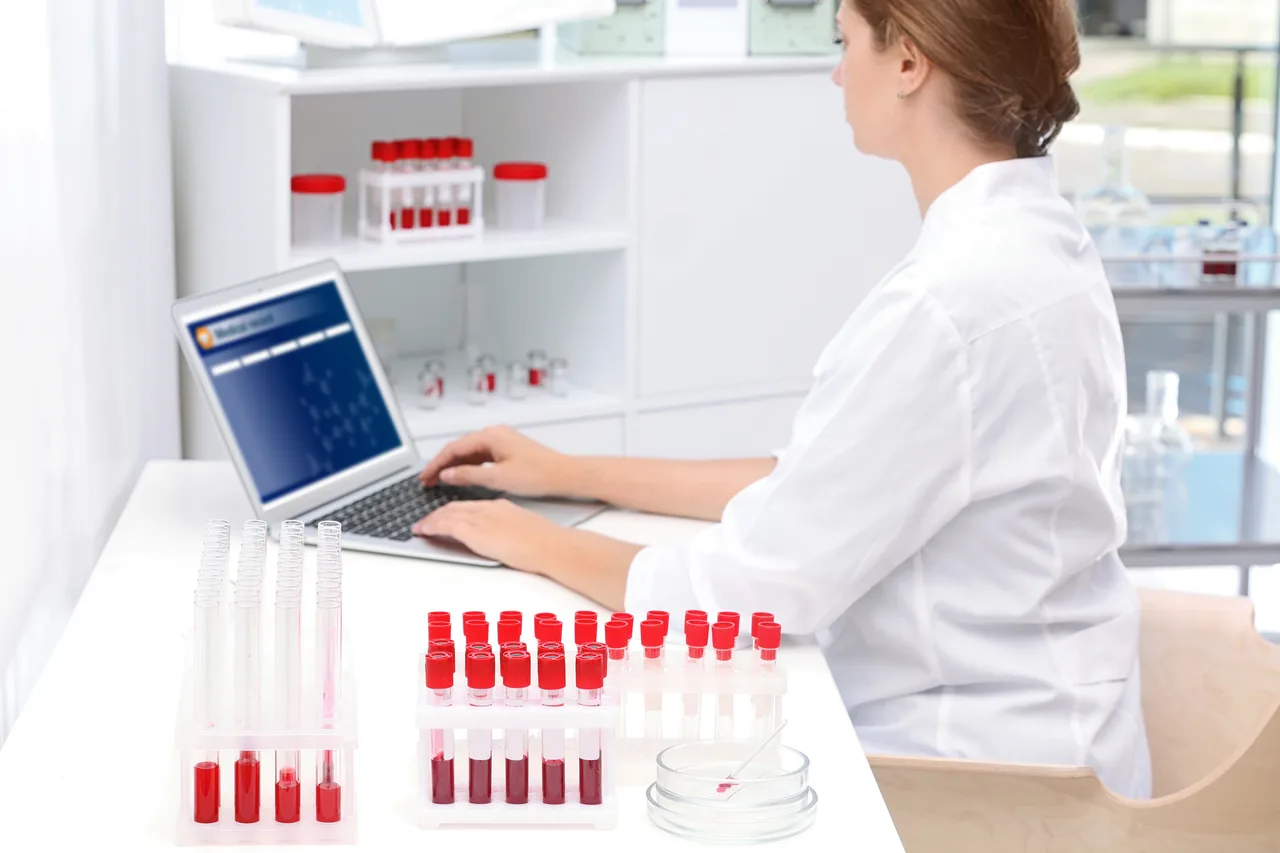 A laboratory analyst recording results on a laptop beside sample tubes