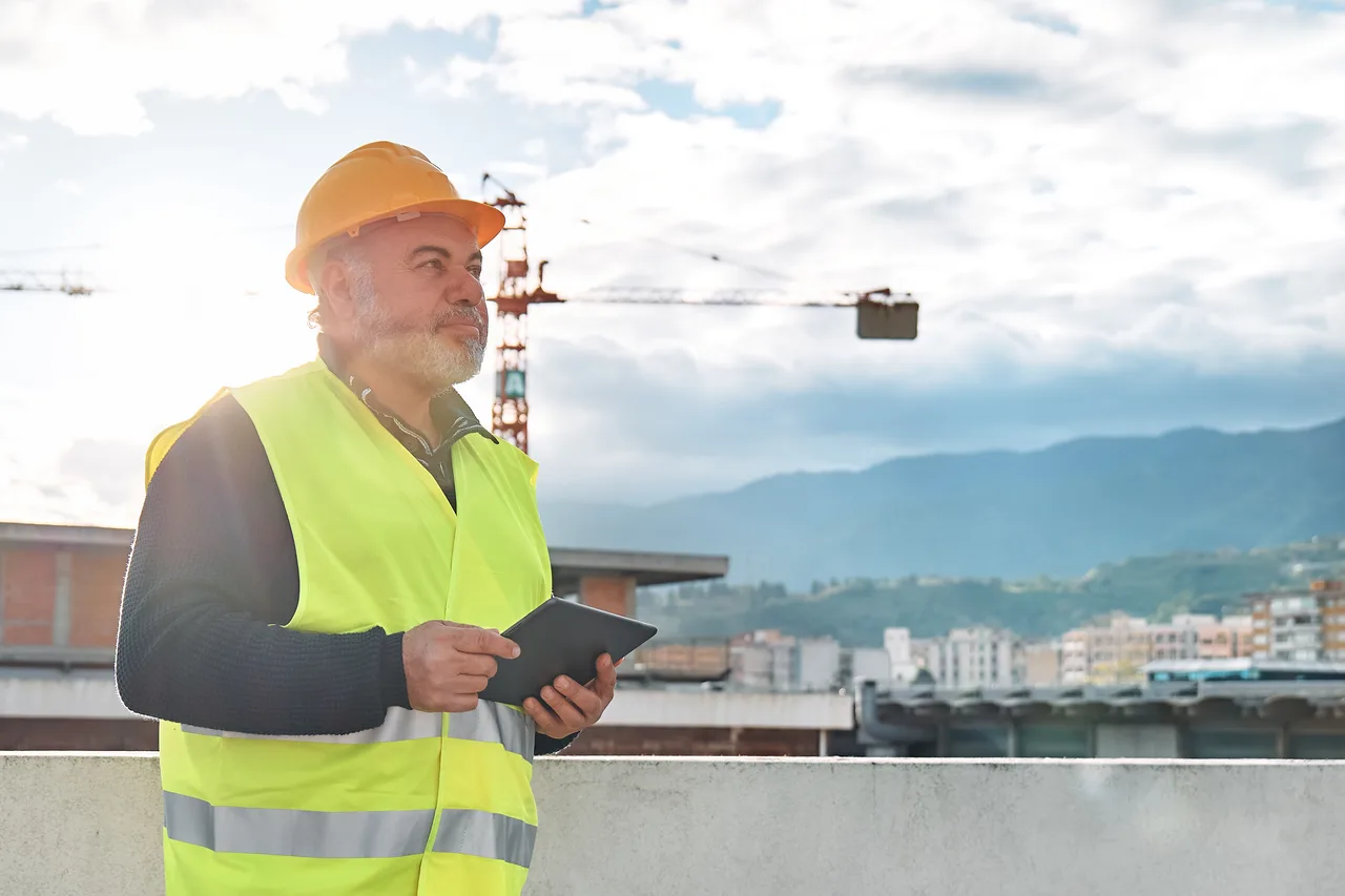 A site supervisor in a safety vest checking a tablet beside a new building