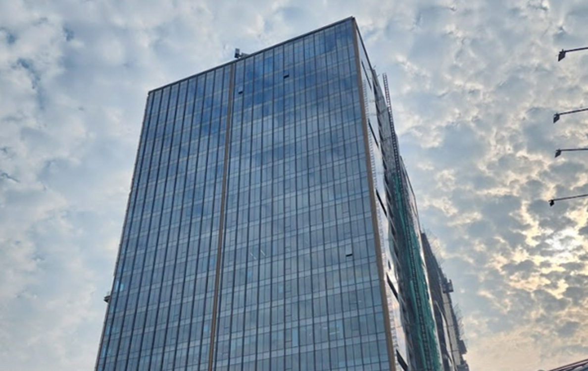 A glass-fronted office tower seen from below against a cloudy sky