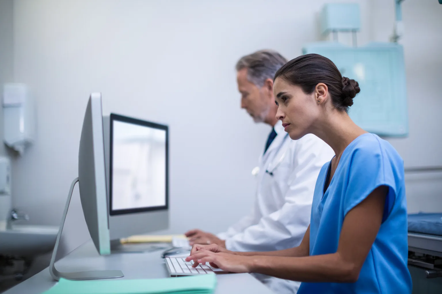 A nurse and a doctor working side by side at hospital computers