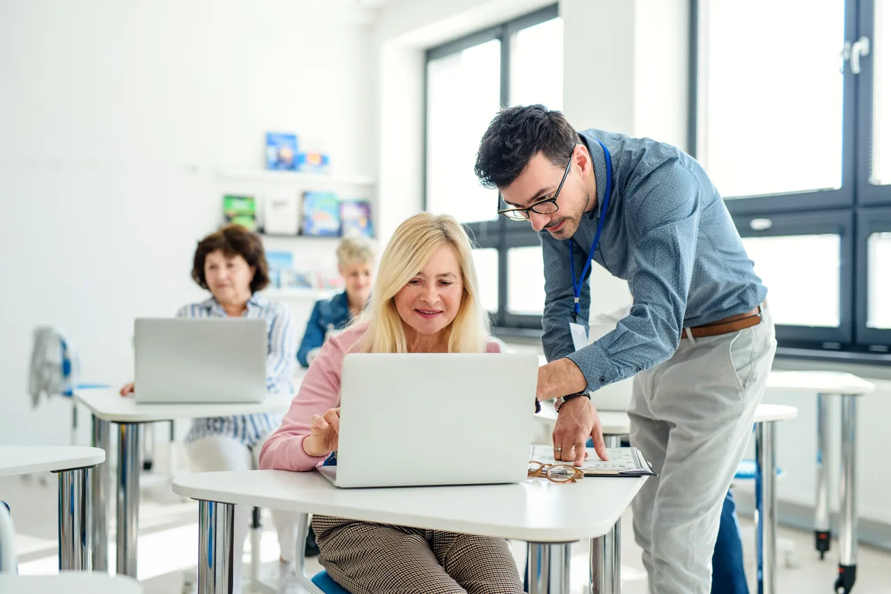 An instructor helping an adult learner at a computer in a training class