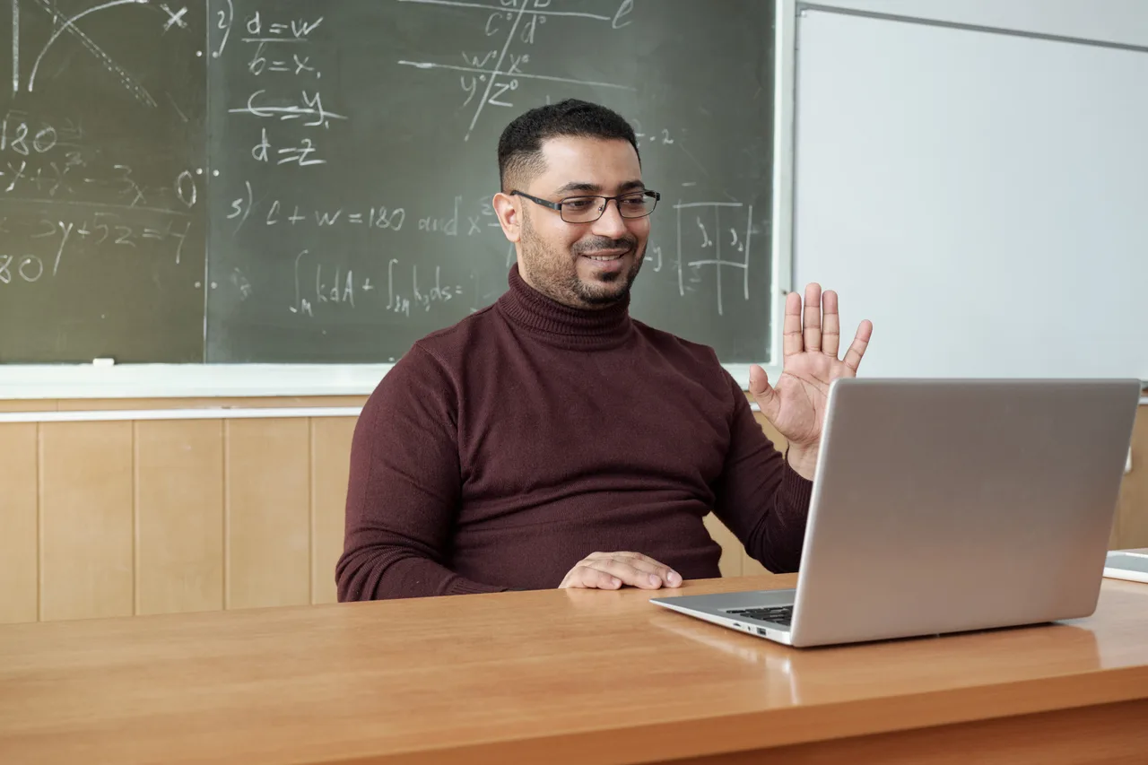 A teacher running an online maths lesson from a classroom desk