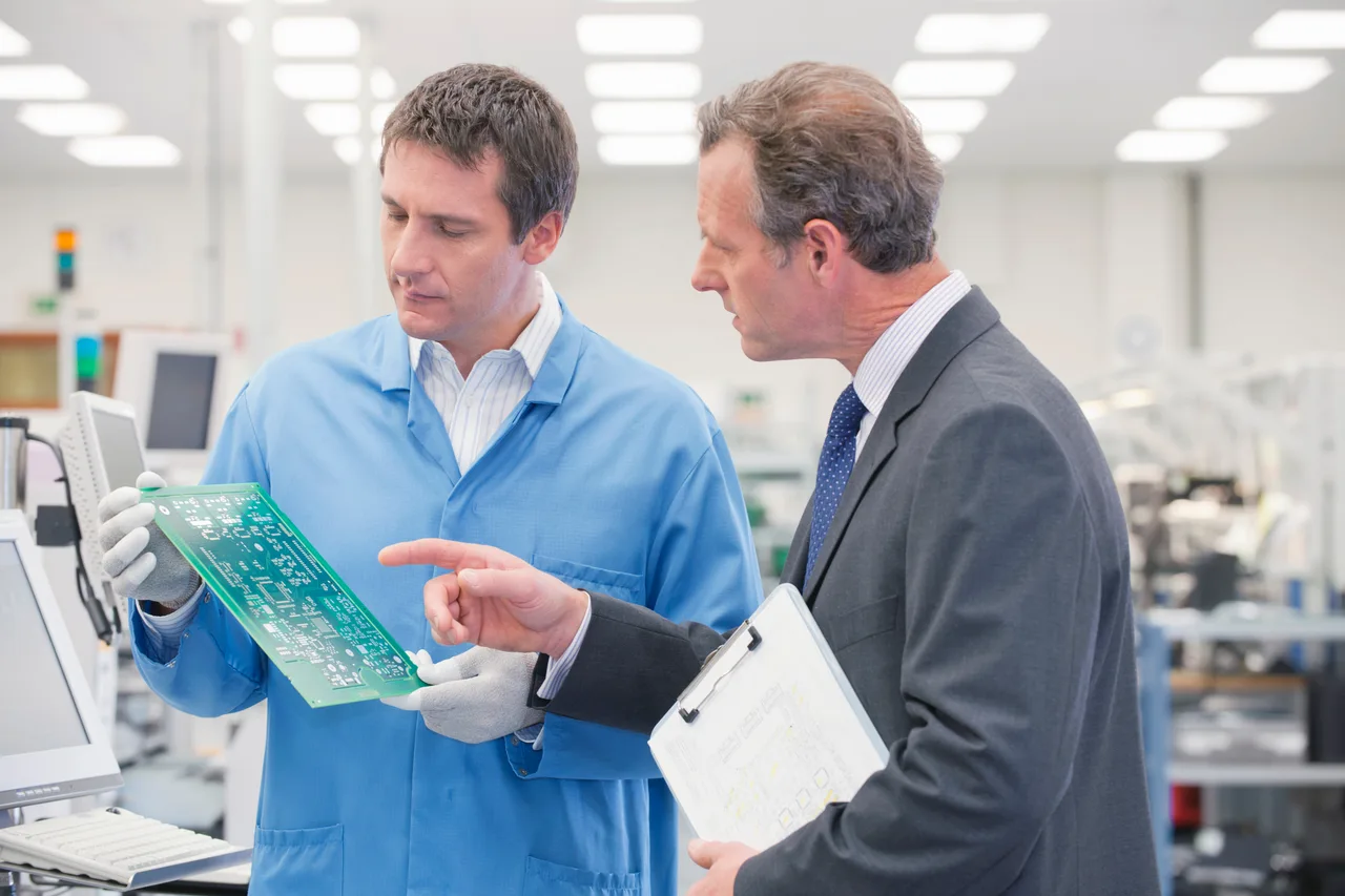 Two engineers inspecting a circuit board in a factory