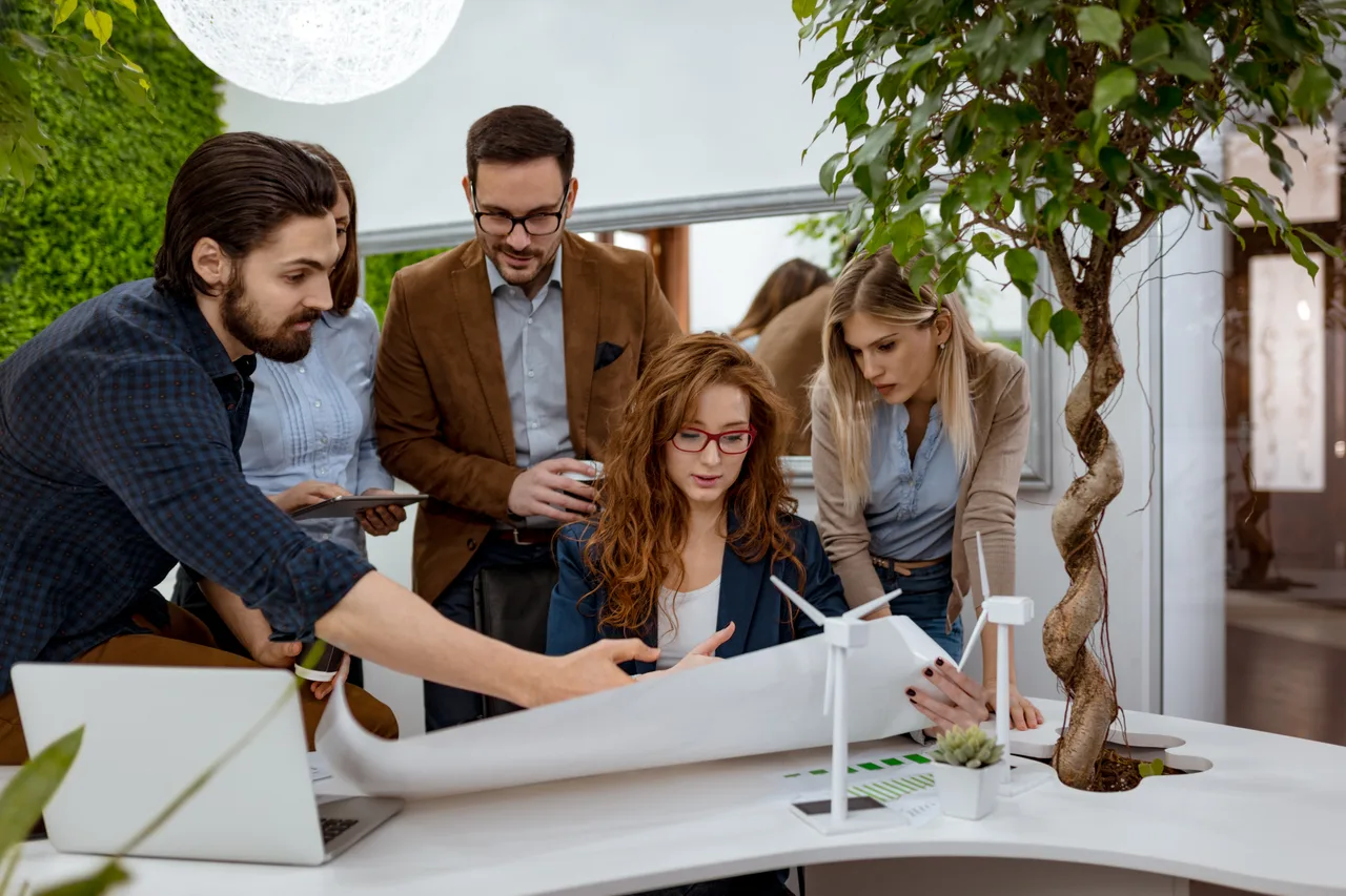 An energy project team reviewing plans beside a wind turbine model