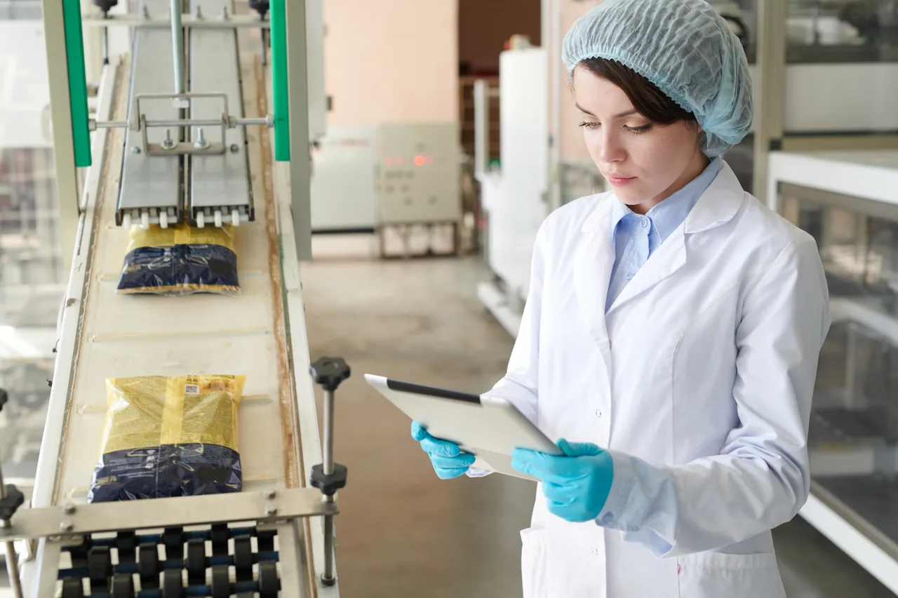 A quality inspector with a tablet beside a food packaging conveyor