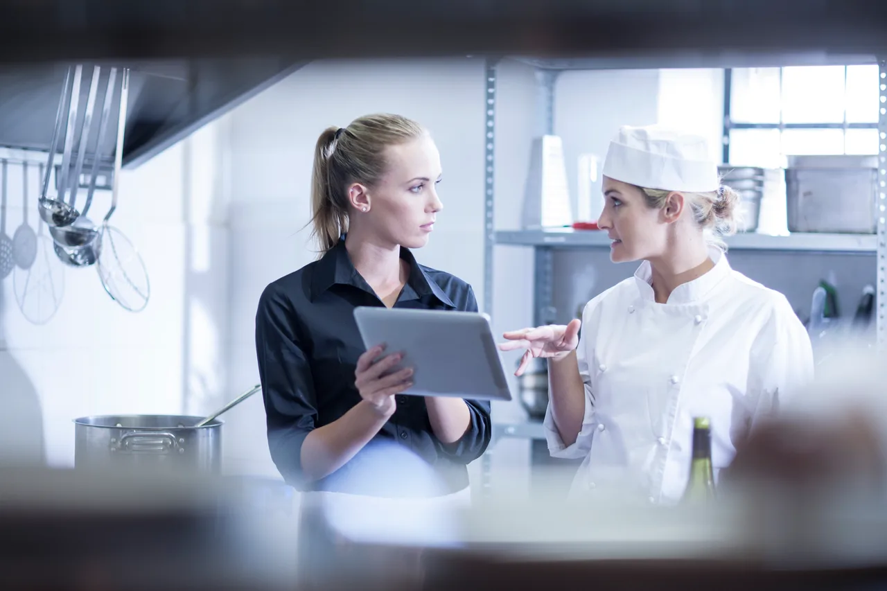 A restaurant manager and a chef reviewing a tablet in a commercial kitchen