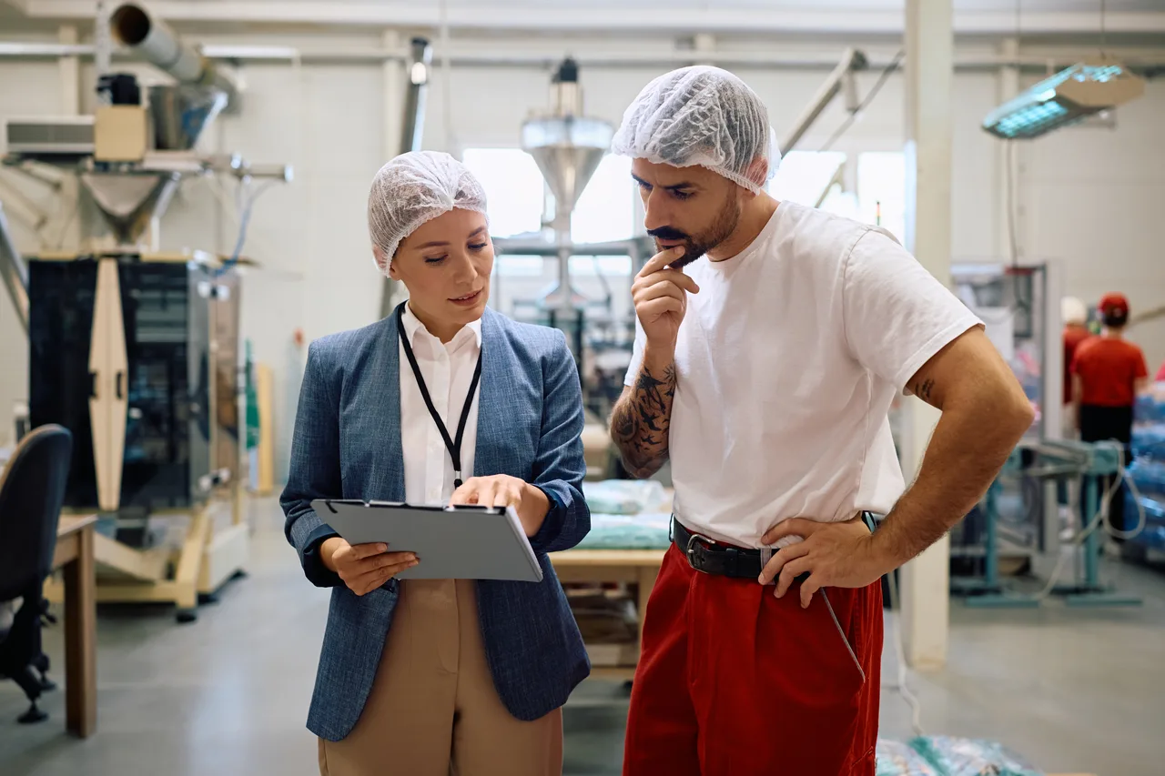 A manager and a production worker reviewing a clipboard on the factory floor