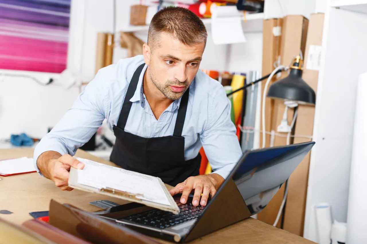 A small-business owner working through paperwork at a laptop