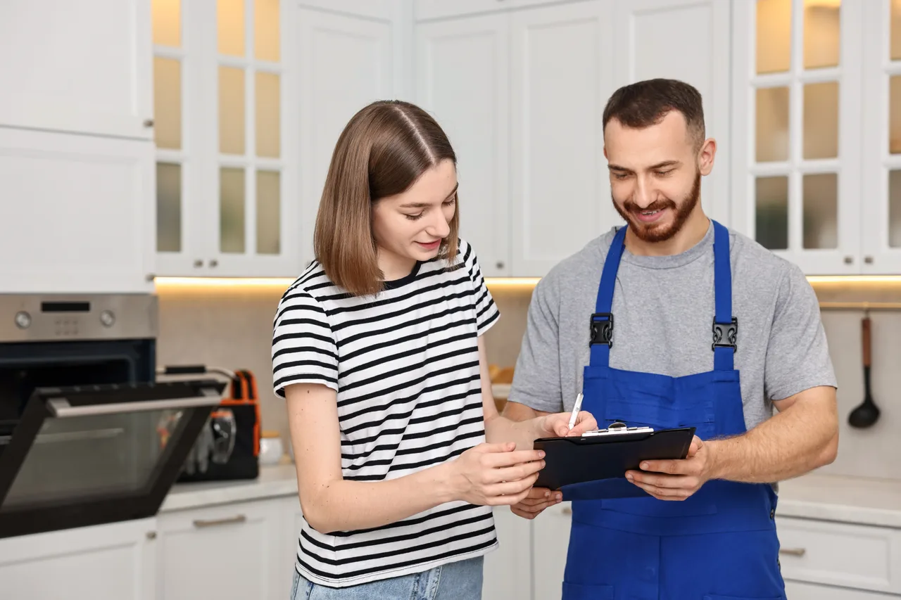 A repair technician going over job details with a customer in her kitchen