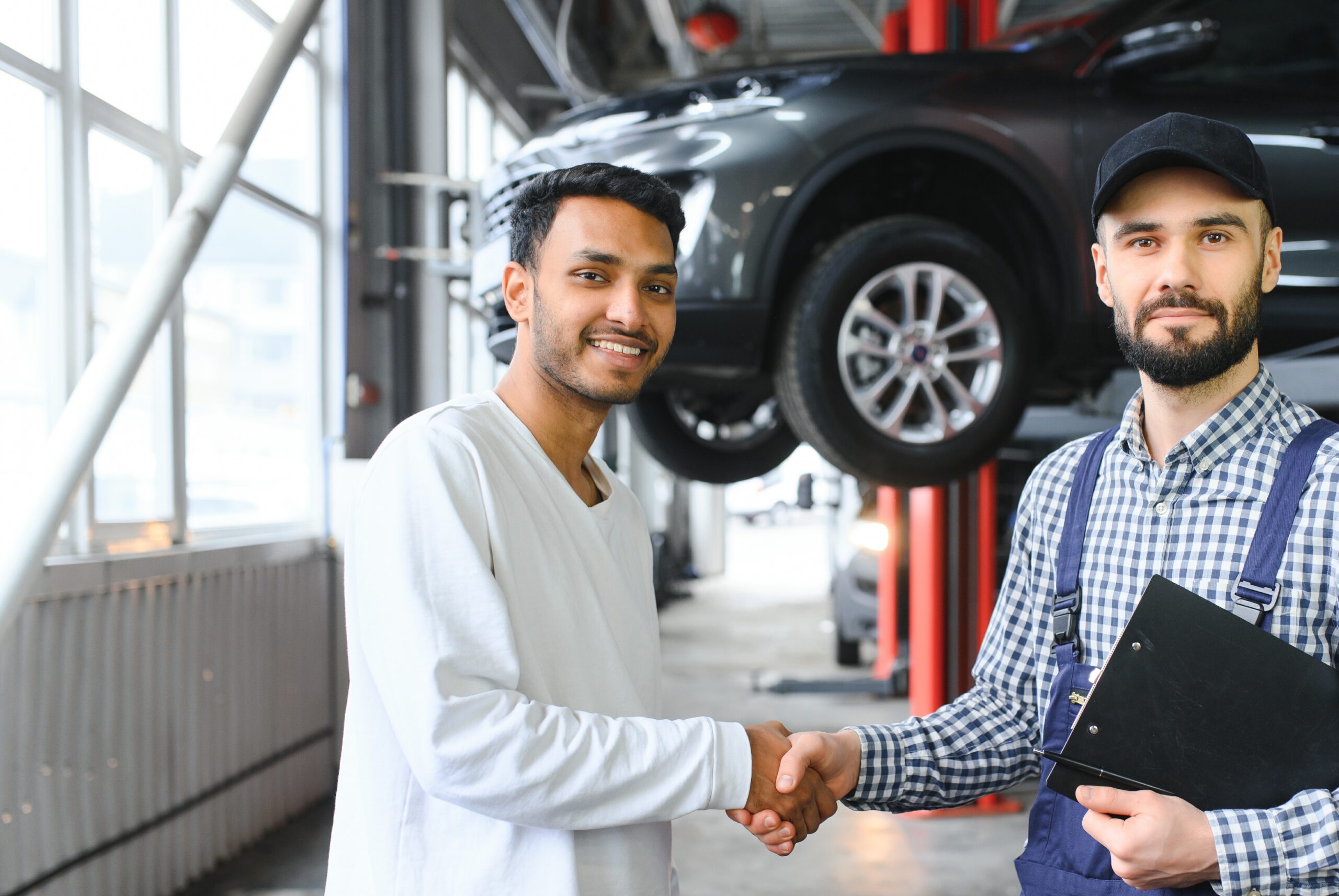 A customer shaking hands with a mechanic in a service workshop, with a car raised on a lift behind them