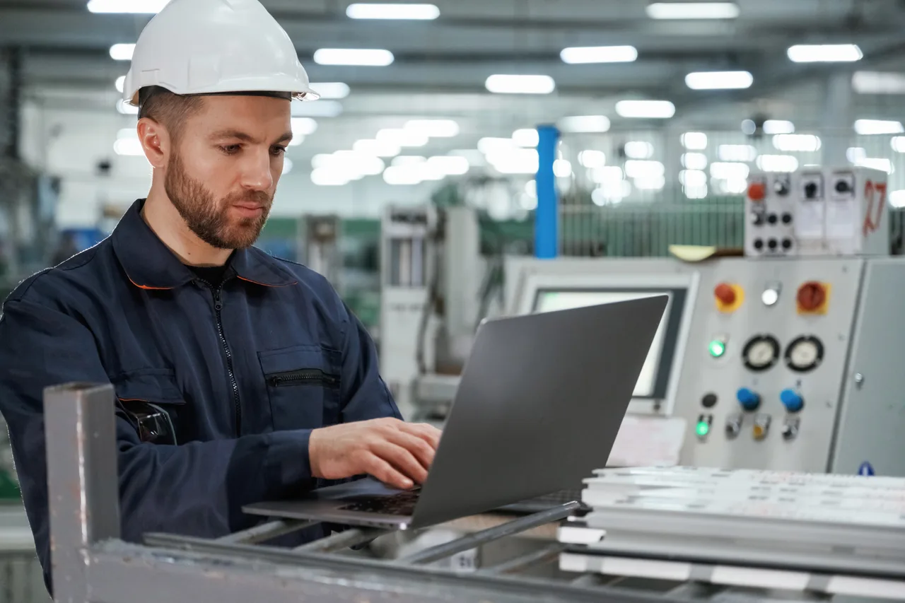 An engineer working on a laptop beside a machine control panel