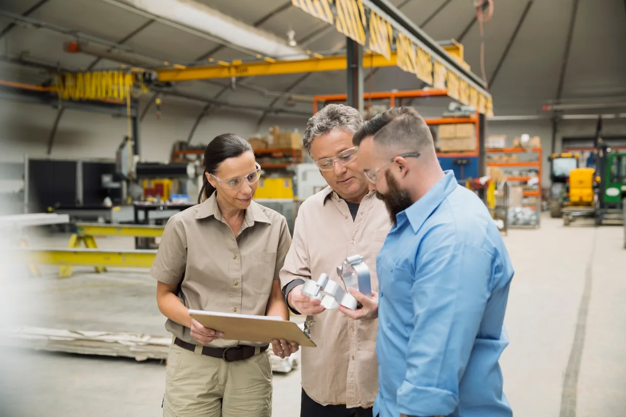 Three colleagues inspecting a machined part in a manufacturing facility