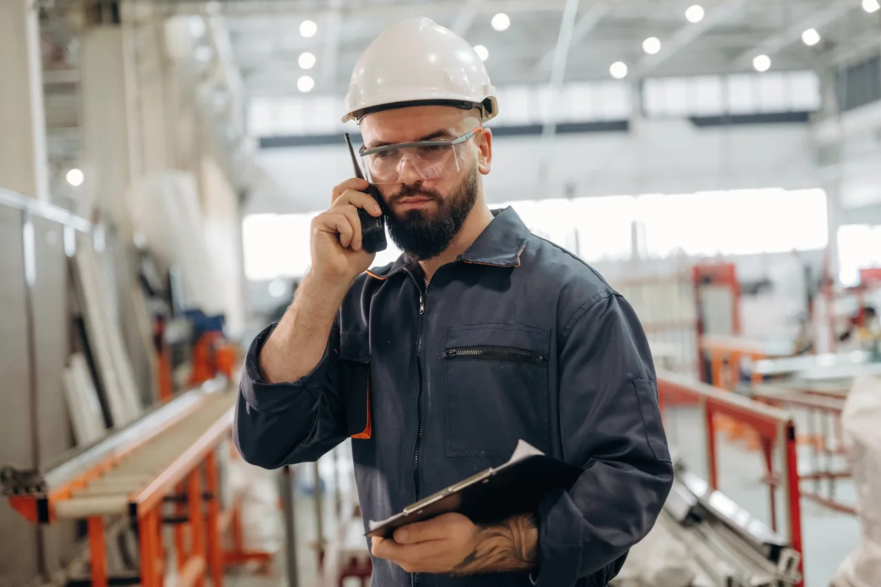 A plant engineer on a call with a clipboard on the factory floor