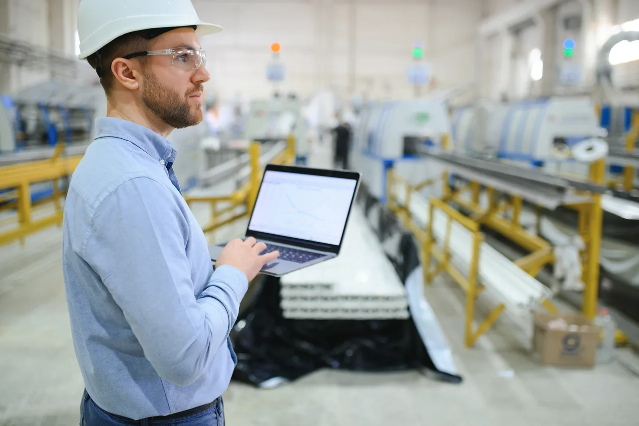 A production engineer with a laptop inspecting a factory line