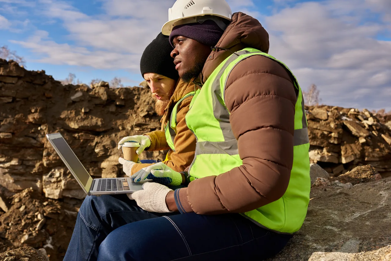 Two engineers reviewing plans on a laptop at a rocky site