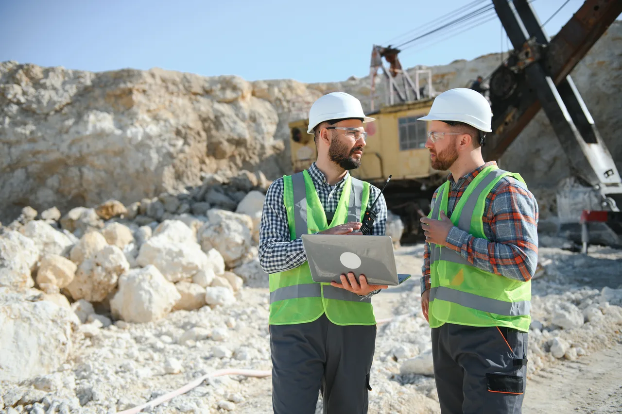 Two mine engineers reviewing a laptop at a quarry