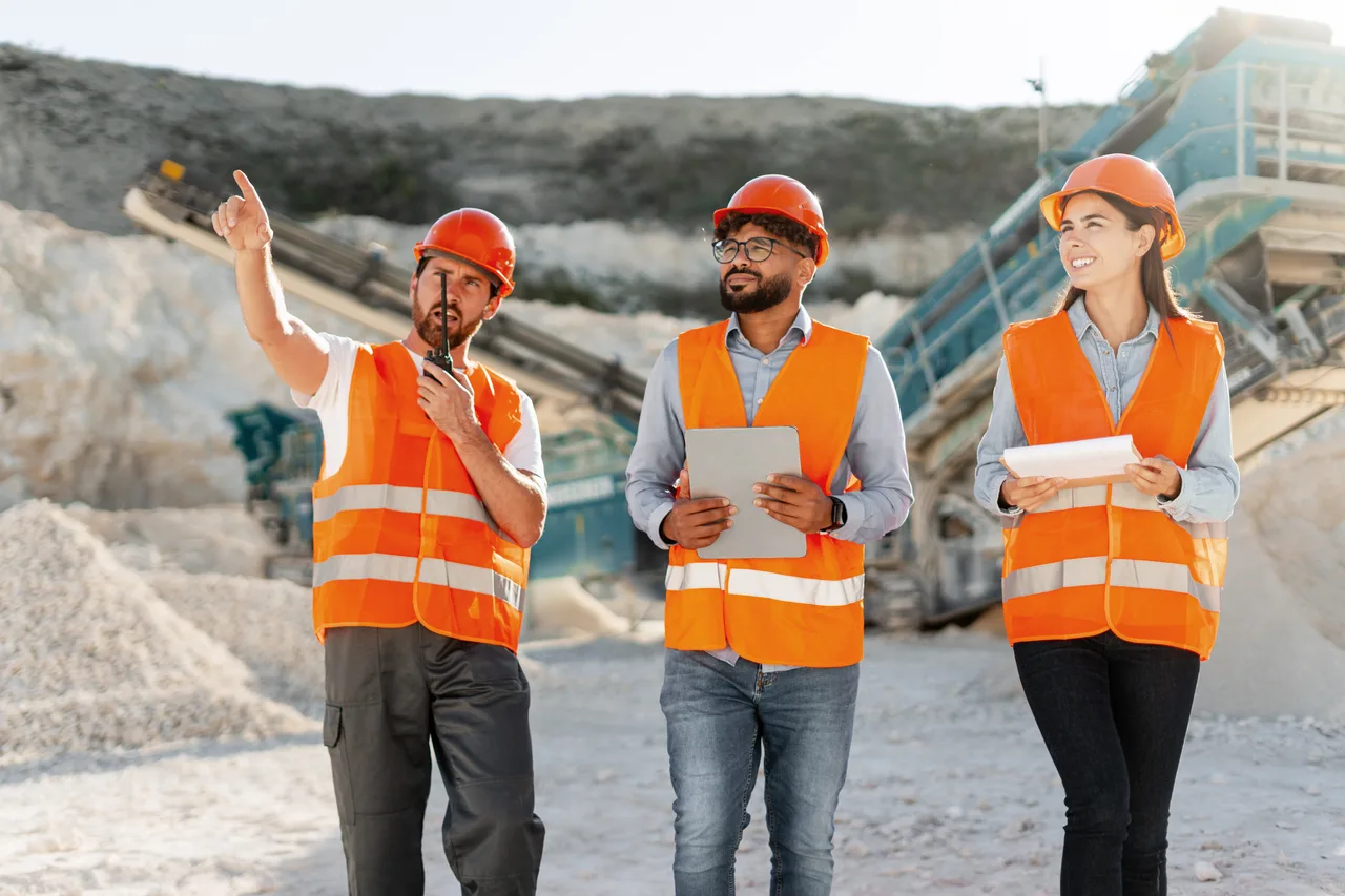Three site workers surveying a quarry with equipment