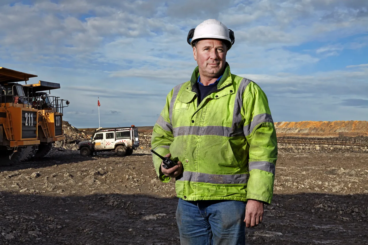 A mine worker standing beside a line of haul trucks