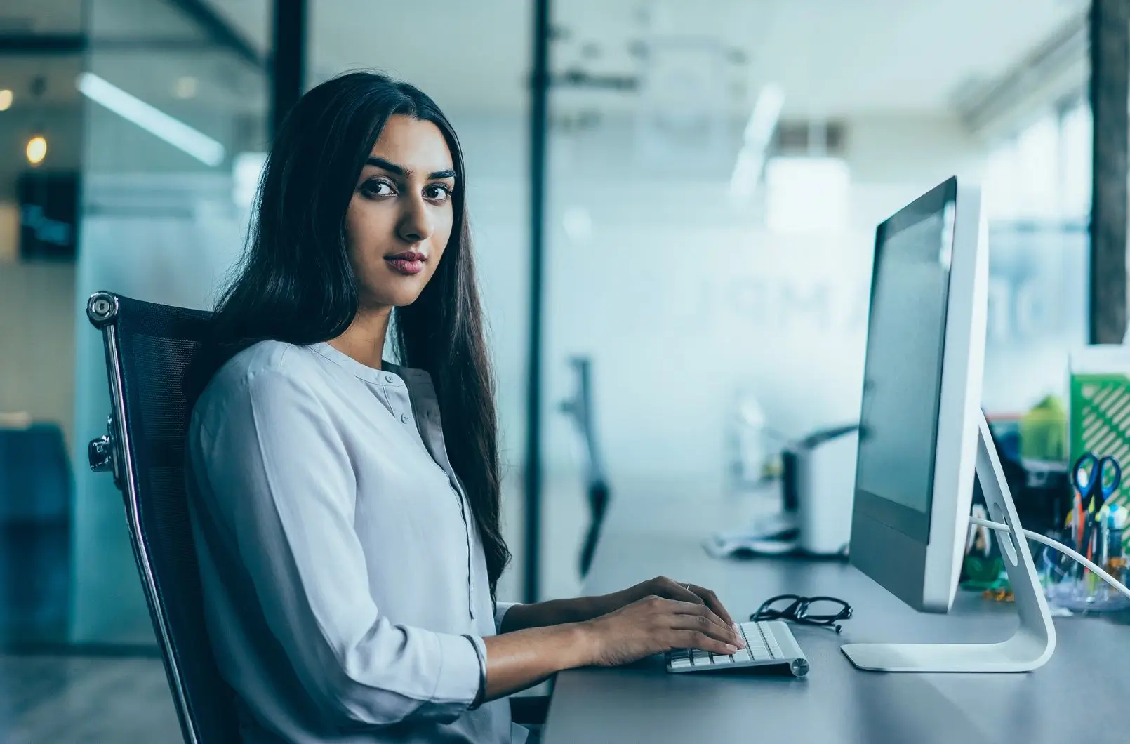 A woman at an office desk typing on a desktop computer