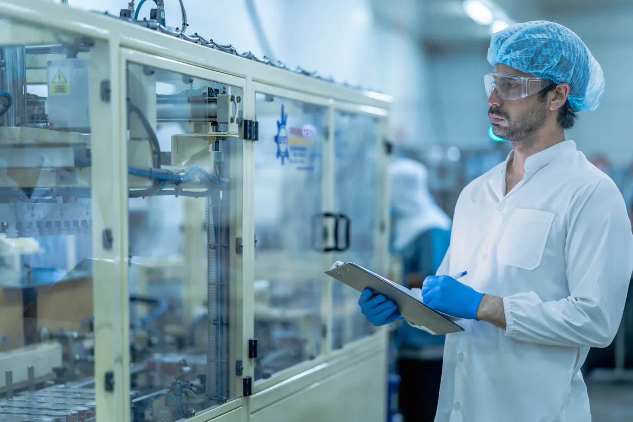 A technician in a lab coat and hairnet inspecting a production line