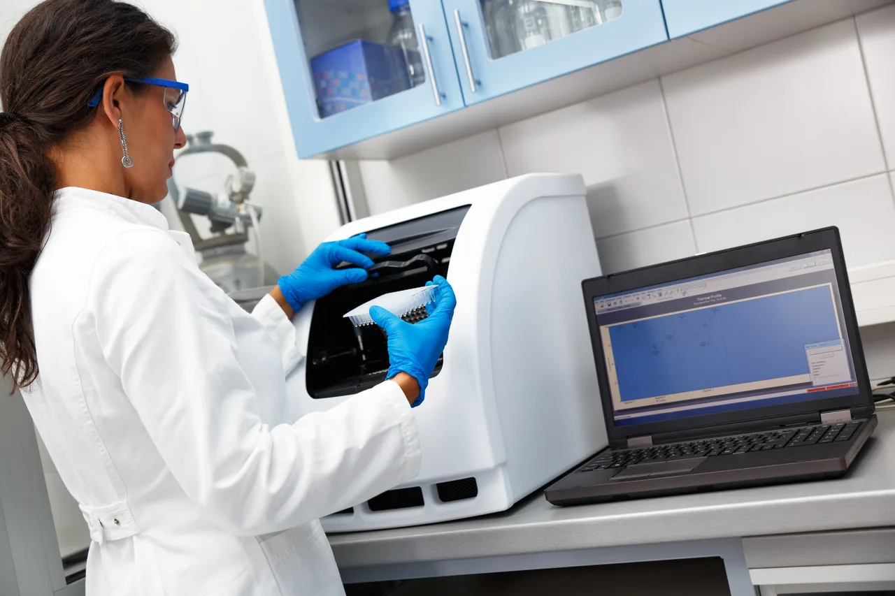 A laboratory technician loading an analyser beside a laptop