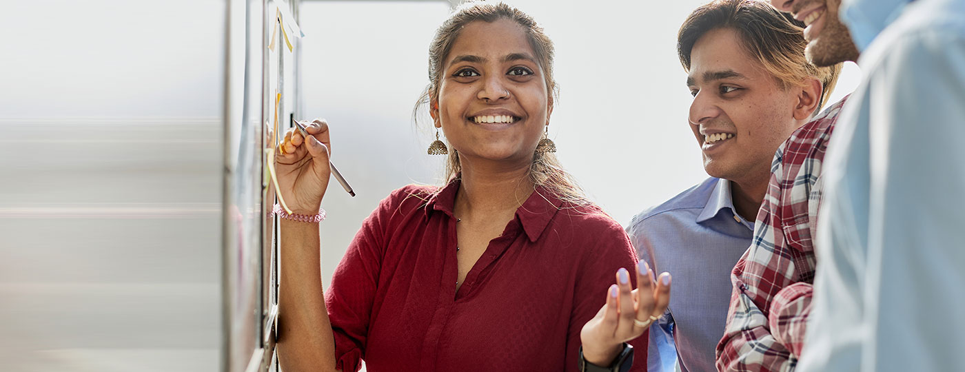 A smiling woman with a pen at a wall of sticky notes while two colleagues look on