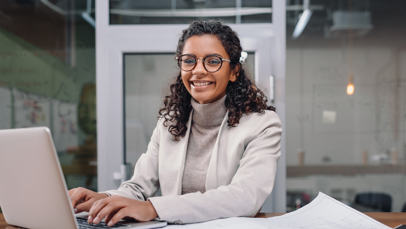 A smiling woman in glasses typing at a laptop in an office