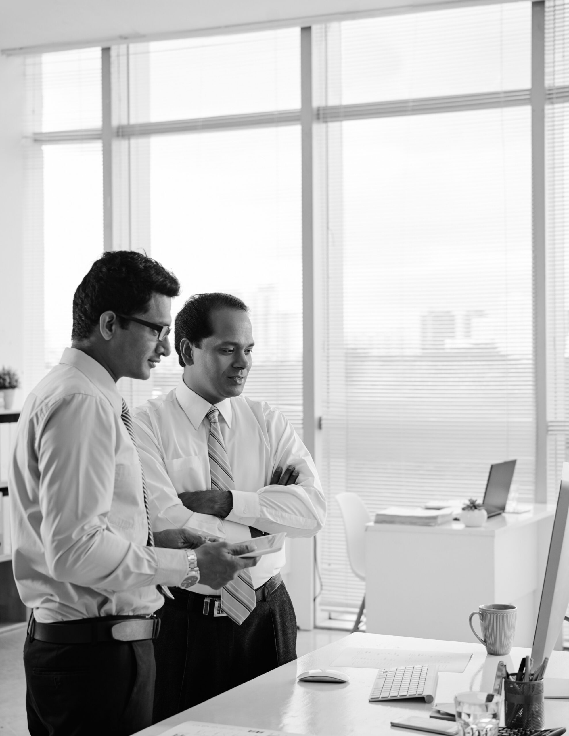 Two colleagues in shirts talking beside an office window, in black and white